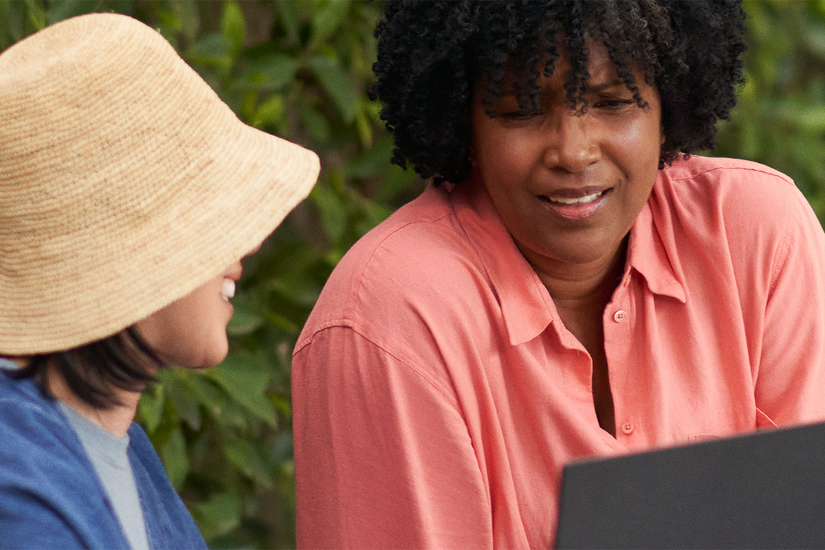 Dos mujeres conversan mientras utilizan un ordenador portátil de PCSpecialist con Windows 11